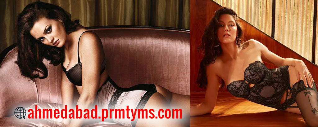 Two women in lingerie posing indoors, one reclining on a sofa in a pink and black set and the other leaning on a wooden floor in black lace lingerie, with text 'ahmedabad.prmtyms.com' displayed.